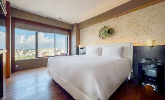 a large white bed with wooden floors is in a room with a window overlooking a cityscape at Hyatt Regency Naha, Okinawa