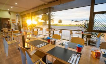 a restaurant with wooden tables and chairs , set up for dining , has a view of the ocean at Hospitality Esperance, SureStay Collection by Best Western