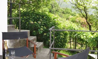 a balcony overlooking a lush green garden , with two chairs and a bottle of wine placed on the edge at Bellavista