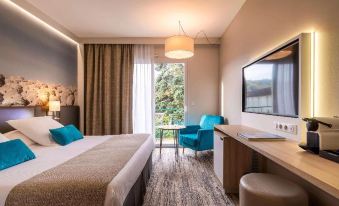 a hotel room with a bed , desk , and chair is shown with a view of the outdoors at Mercure Castres l'Occitan