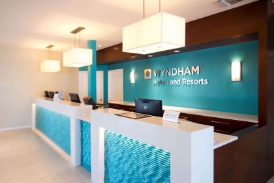 a reception desk with a laptop on it , and a blue wall behind it displaying the wyndham logo at Wyndham Reef Resort Grand Cayman