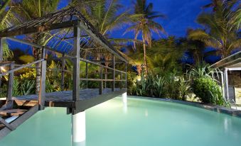 a large swimming pool with a wooden deck and an umbrella is surrounded by palm trees at Likuri Island Resort Fiji