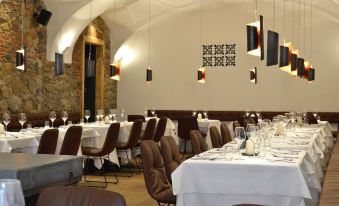 a large dining room with multiple tables and chairs , white tablecloths , and hanging light fixtures at Hotel Maribor & Garden Rooms