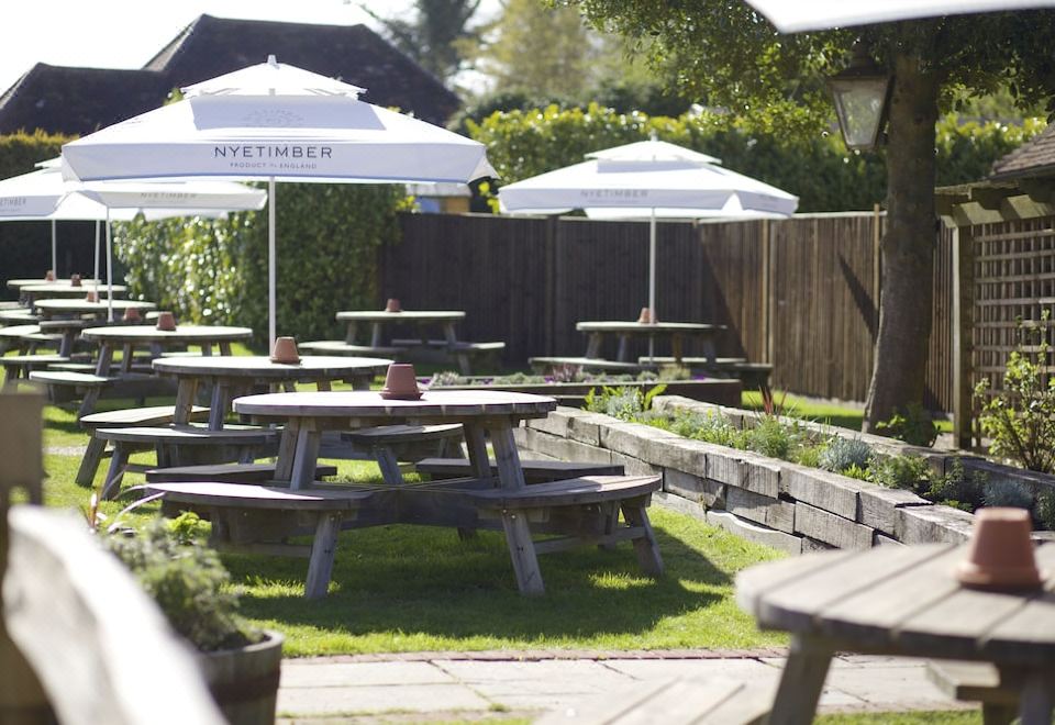 an outdoor dining area with multiple tables and chairs under white umbrellas , surrounded by greenery at The Woolpack Inn