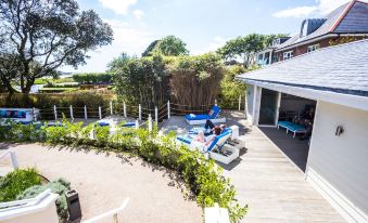 a patio with blue chairs and a dining table , surrounded by lush greenery and a wooden fence at Harbour Hotel & Spa Christchurch