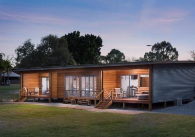 a wooden house surrounded by grass and trees , with a deck on the left side at The Swan Valley Retreat