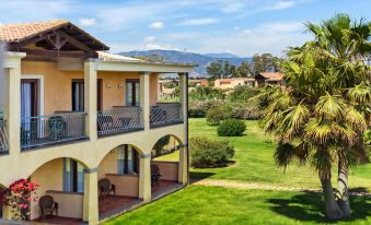 a beautiful villa with a large grassy area and palm trees , surrounded by mountains in the background at Hotel Santa Gilla