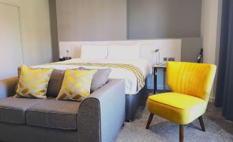 a bed with yellow pillows and a gray couch , next to a yellow chair in a bedroom at Mode Hotel Lytham