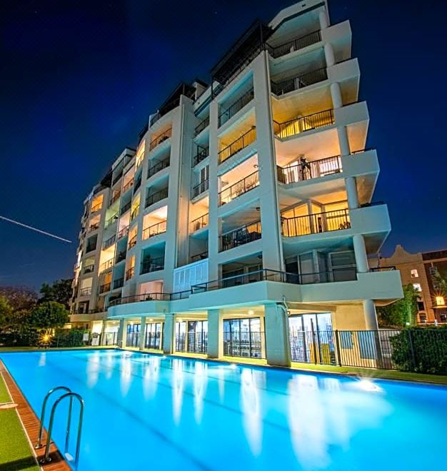 a modern apartment building with a swimming pool in front of it at night , illuminated by lights at Goldsborough Place Apartments