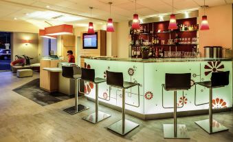 a modern bar area with multiple chairs and stools , as well as a tv mounted on the wall at Ibis Clermont-Ferrand Sud Carrefour Herbet