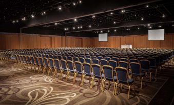 a large conference room with rows of blue chairs and a screen at the front at Hilton Newcastle Gateshead