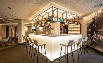 a modern bar with a long wooden counter , several stools , and shelves filled with various bottles at Hotel HerzogsPark