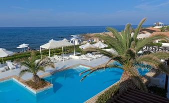 a resort with a large pool surrounded by lounge chairs and umbrellas , overlooking the ocean at Aldemar Knossos Royal