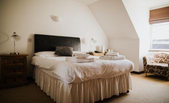 a white bed with a black headboard and white sheets is in a room with a slanted ceiling at The Stratton House Hotel