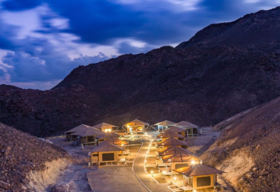 a dirt road in the mountains , with several small buildings scattered throughout the area , illuminated by lights at Ras Al Jinz Turtle Reserve