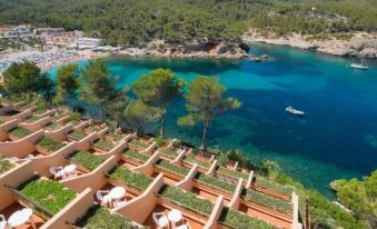 a resort with a large pool surrounded by green trees and a body of water in the background at Ole Galeon Ibiza