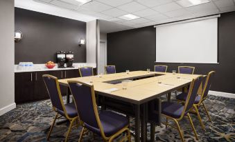 a conference room with a wooden table surrounded by blue chairs and a projector screen at Residence Inn Philadelphia Langhorne