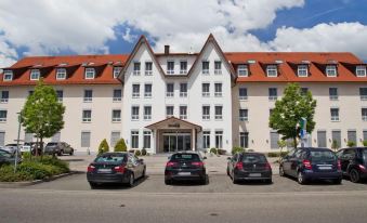 a large white building with a red roof is surrounded by four cars parked in front at Fairway Hotel