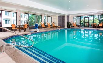 an indoor swimming pool with a clear blue water , surrounded by chairs and sun loungers at Rochester Airport Marriott