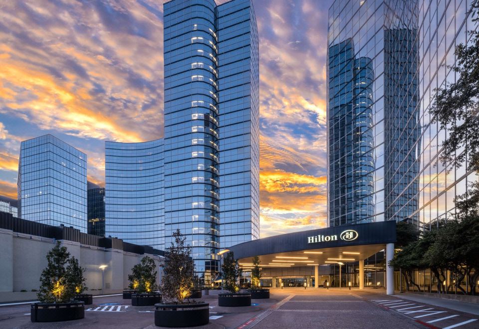 a modern hotel building with tall windows and a unique curved design is surrounded by other buildings in the city at Hilton Dallas Lincoln Centre