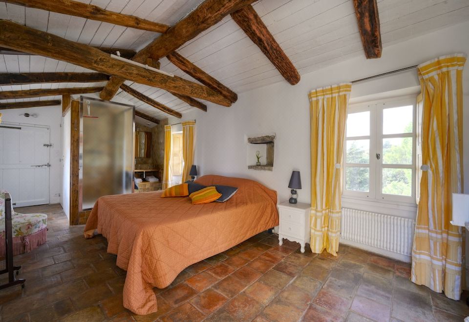 a spacious bedroom with wooden beams on the ceiling , a large bed , and a bathroom adjacent to it at Chambre d'Hotes
