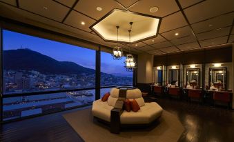 a modern living room with a large window offering a view of the city , a comfortable seating area with cushions , and several dining tables at La Vista Hakodate Bay