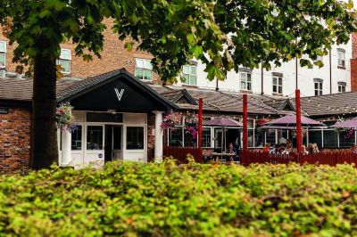 a row of restaurants with black and white exterior doors , surrounded by trees and a brick building at Village Hotel Liverpool