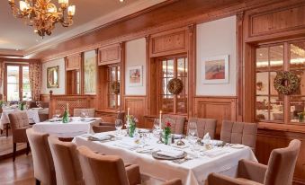 a restaurant with wooden walls , large windows , and a chandelier , featuring multiple dining tables set for guests at Schlosshotel Fiss