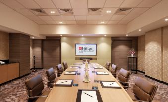 a large conference room with a long table , chairs , and a screen displaying the hilton garden inn logo at Hilton Garden Inn Puchong