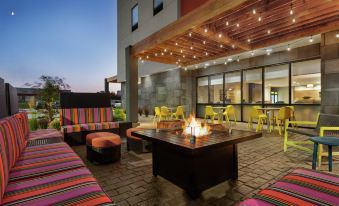 a brick patio with a fire pit surrounded by colorful chairs and a bar in the background at Home2 Suites by Hilton Dekalb