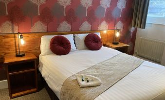 a large bed with white linens and two red pillows is in a room with wooden headboards at The Bulls Head