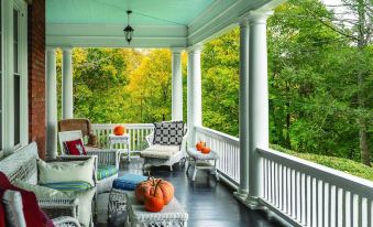 a porch with a white railing and multiple chairs , two ottomans , and a ceiling adorned with pumpkins at Hillcrest Mansion Inn