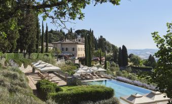 a large villa with a pool is surrounded by trees and lounge chairs on a hillside at Rosewood Castiglion del Bosco