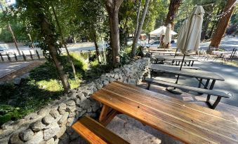 a wooden picnic table surrounded by trees , with a stone wall in the background and an outdoor dining area nearby at The Historic Brookdale Lodge, Santa Cruz Mountains