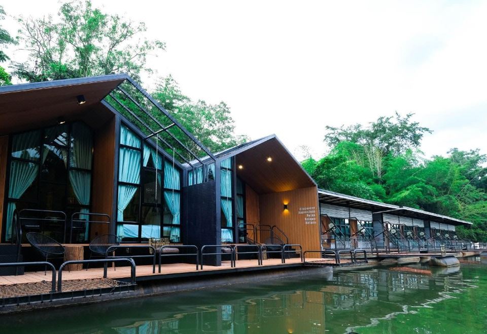 a modern building with large windows and wooden doors , situated on the edge of a river surrounded by trees at Baan Rai Darun Home Stay and Scenery Raft