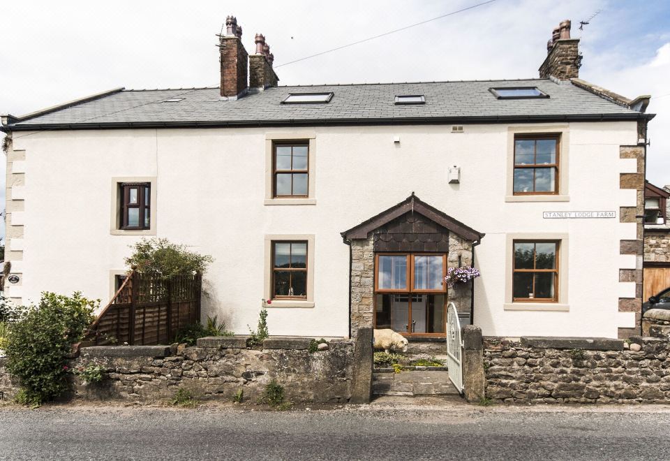 a white house with a stone wall and a black roof is shown in the image at Stanley Lodge Farmhouse