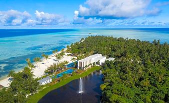 aerial view of a tropical beach resort with a pool , surrounded by lush greenery and palm trees at Pullman Maldives All-Inclusive Resort
