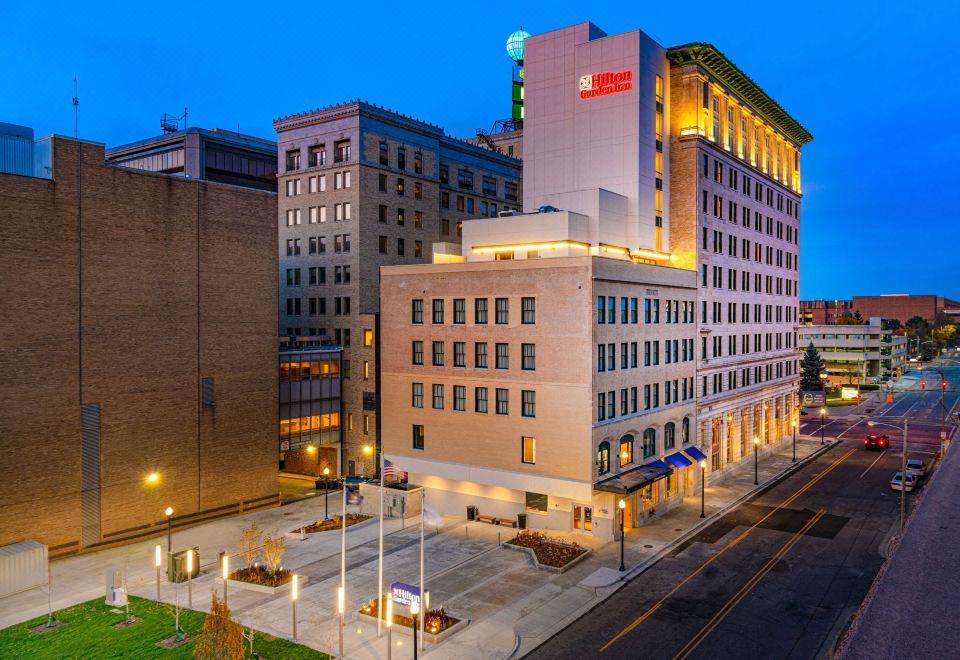 a large building with a red sign is lit up at night , and has a plaza in front of it at Hilton Garden Inn Flint Downtown