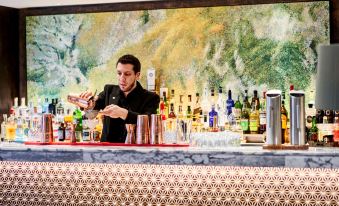 a man is standing behind a bar , preparing a drink with various bottles and glasses at DoubleTree by Hilton Wellington