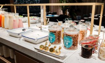 a dining table with a variety of food items , including bowls , cups , and bottles , as well as a bowl of cereal at NH Collection Antwerp Centre
