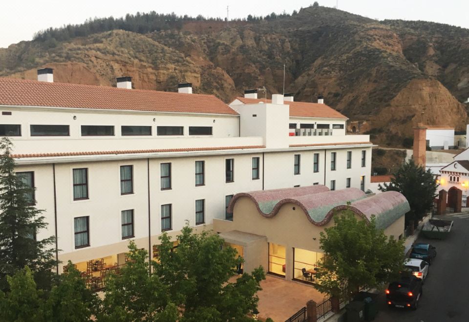 a large white building with red roofs and a curved roof is situated in front of a mountain at Hotel Balneario de Graena
