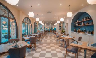 a modern restaurant with white and blue checkered flooring , multiple dining tables , chairs , and potted plants at Megisti Hotel