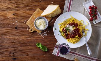 a wooden table with a plate of spaghetti and meat sauce , a bowl of cheese , and a glass of wine at Ibis Firenze Nord Aeroporto