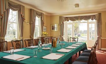 a long dining table set with green tablecloths , surrounded by chairs in a room with windows at Corse Lawn House Hotel