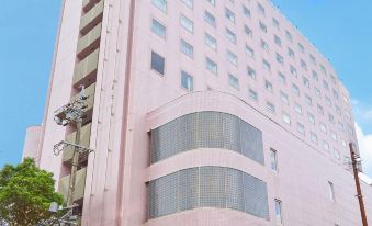 a large pink building with many windows is surrounded by trees and has a parking lot in front at Hotel Resol Gifu