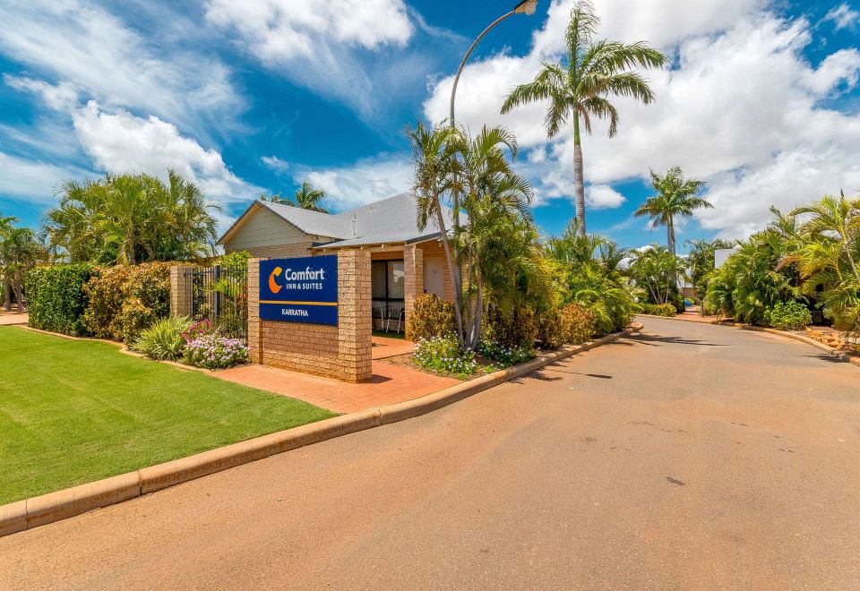 "a small building with a sign that says "" comfort inn "" on it , surrounded by palm trees and grass" at Comfort Inn & Suites Karratha