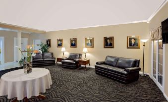 a room with a carpeted floor and black leather couches , tables , and chairs , framed portraits on the walls at Ramada by Wyndham Richland Center