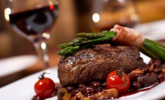 a white plate with a steak and asparagus , accompanied by a glass of wine on a dining table at Hotel Centrale