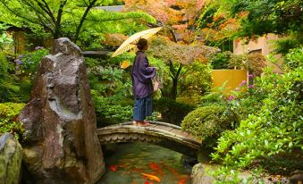 a woman in a purple coat is standing on a stone bridge over a pond filled with goldfish at Fuefukigawa Onsen Zabou