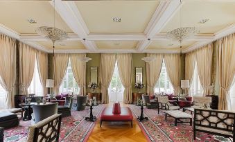 a large , ornate room with a red bench and several chairs arranged around a central table at Vidago Palace